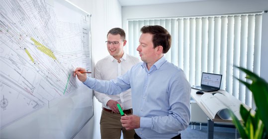 Zwei Männer bei Projektbesprechung an einer Planwand