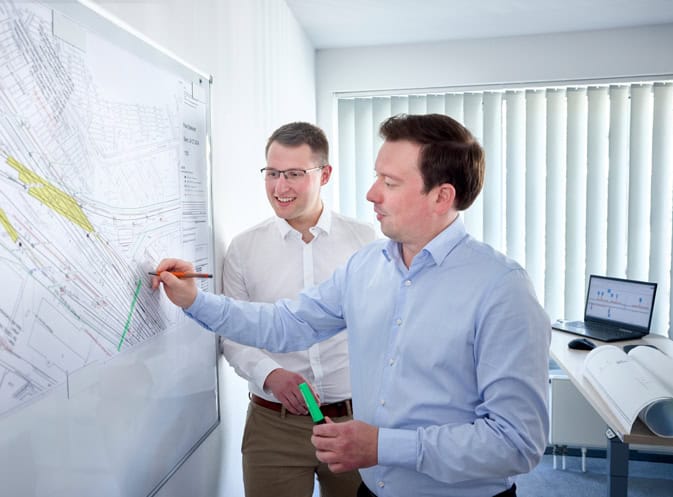 Zwei Männer bei Projektbesprechung an einer Planwand